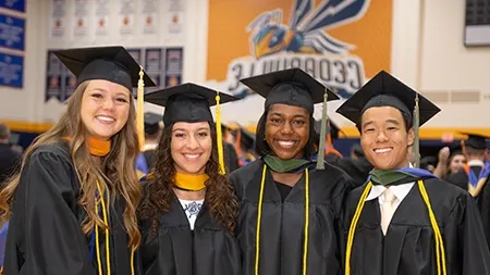 Four students in graduation regalia smiling in gym